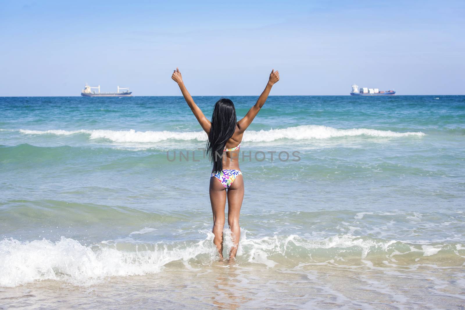 Woman at the beach, hands in the air, looking at the horizon.