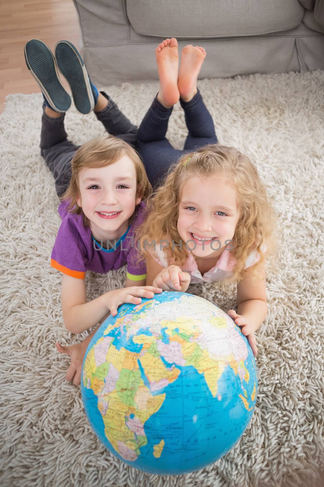 High angle portrait of brother and sister with globe lying on rug at home