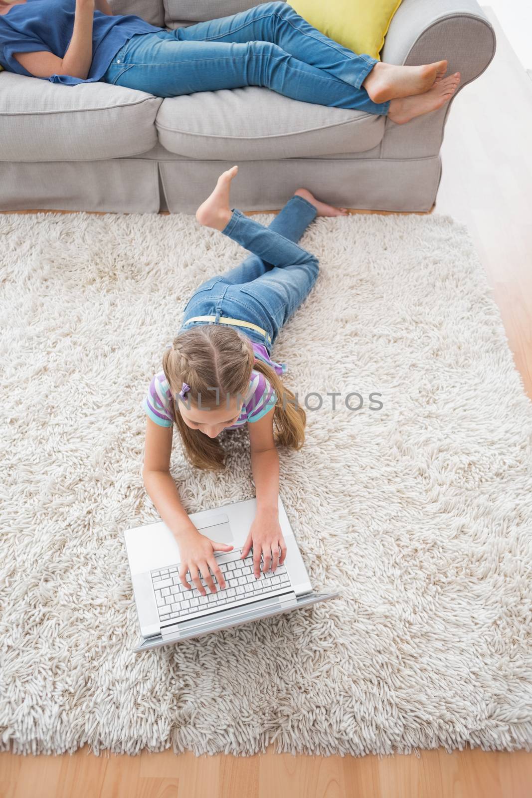 Girl using laptop while lying on rug at home by Wavebreakmedia