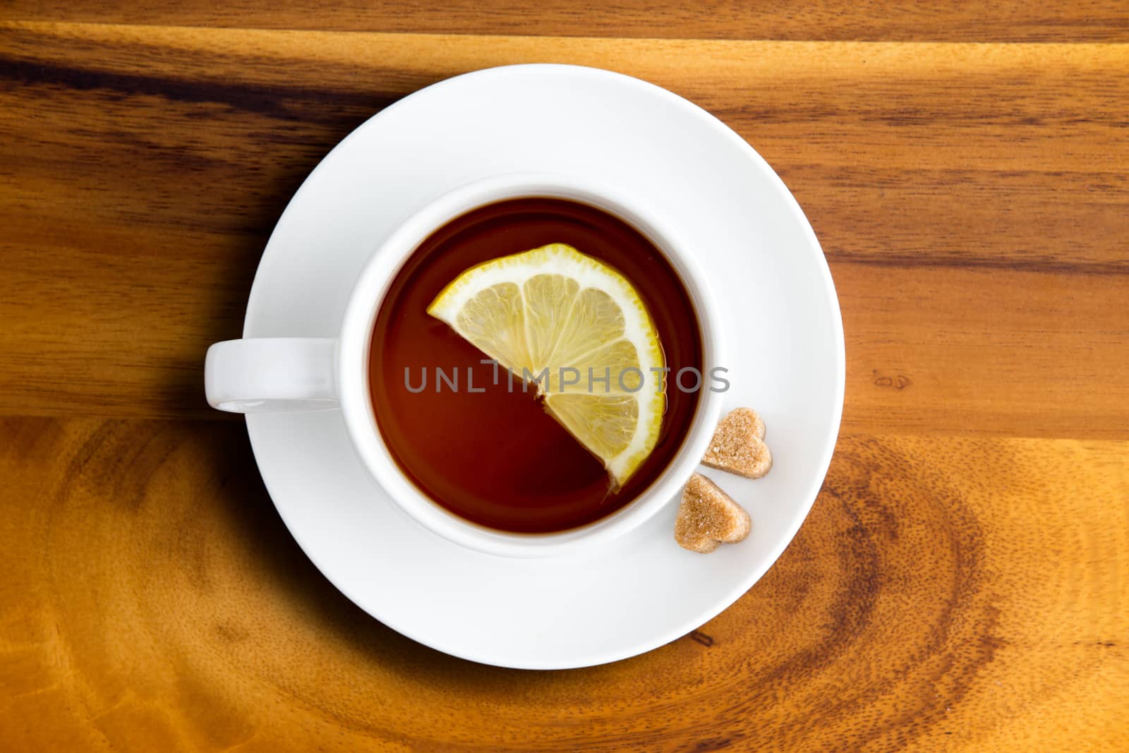 Freshly brewed white cup and saucer of healthy herbal tea with lemon from above with heart shaped brown sugar cubes on a wooden table