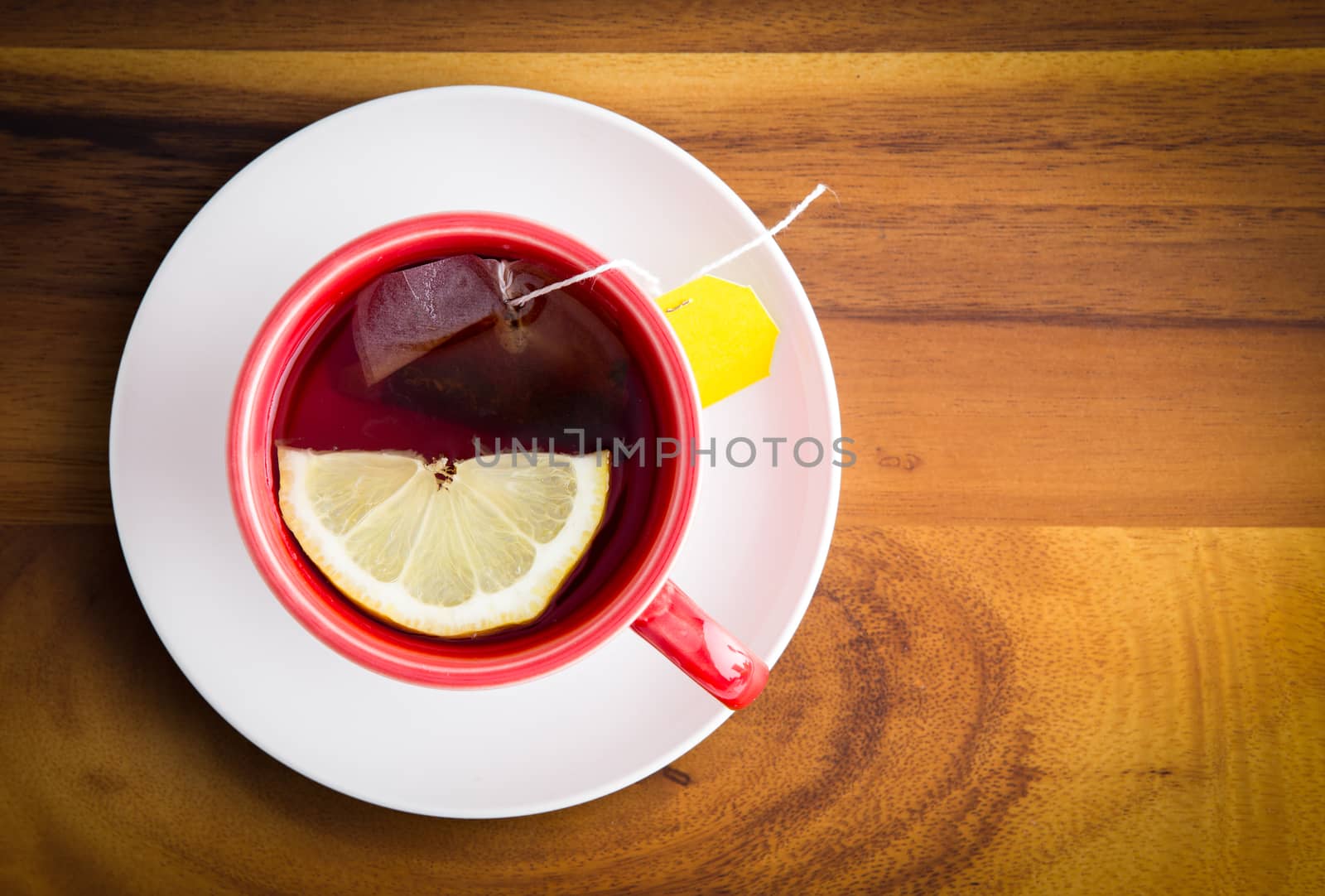 Cup of freshly brewed healthy herbal tea with a lemon slice served in a red cup and white saucer on a wooden table with copyspace, view from above