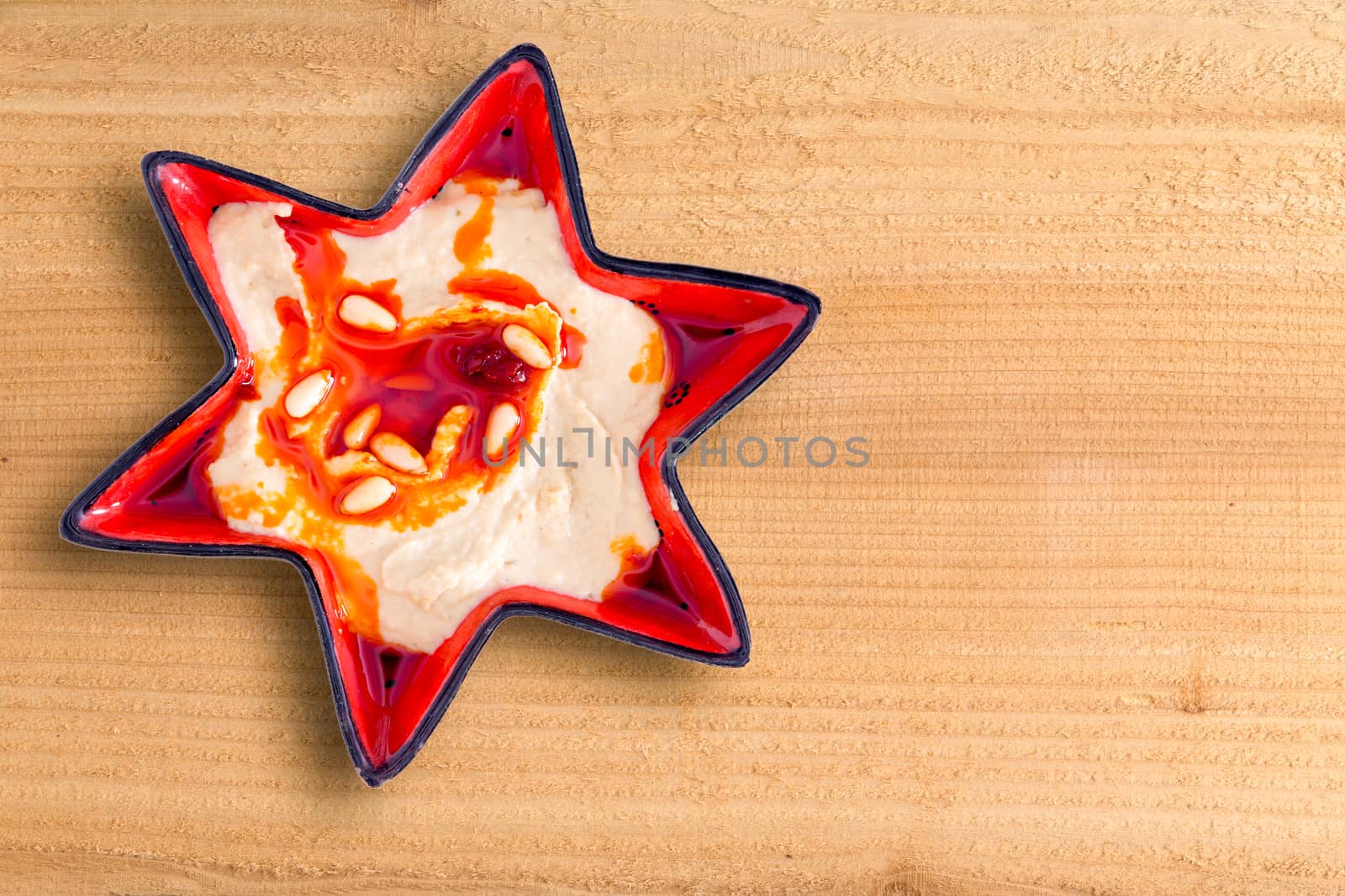 Decortive star-shaped bowl of hummus, a nutritious blend of chickpeas, tahini, oil, lemon juice, and garlic, on a wooden table with copyspace suitable as a Christmas background