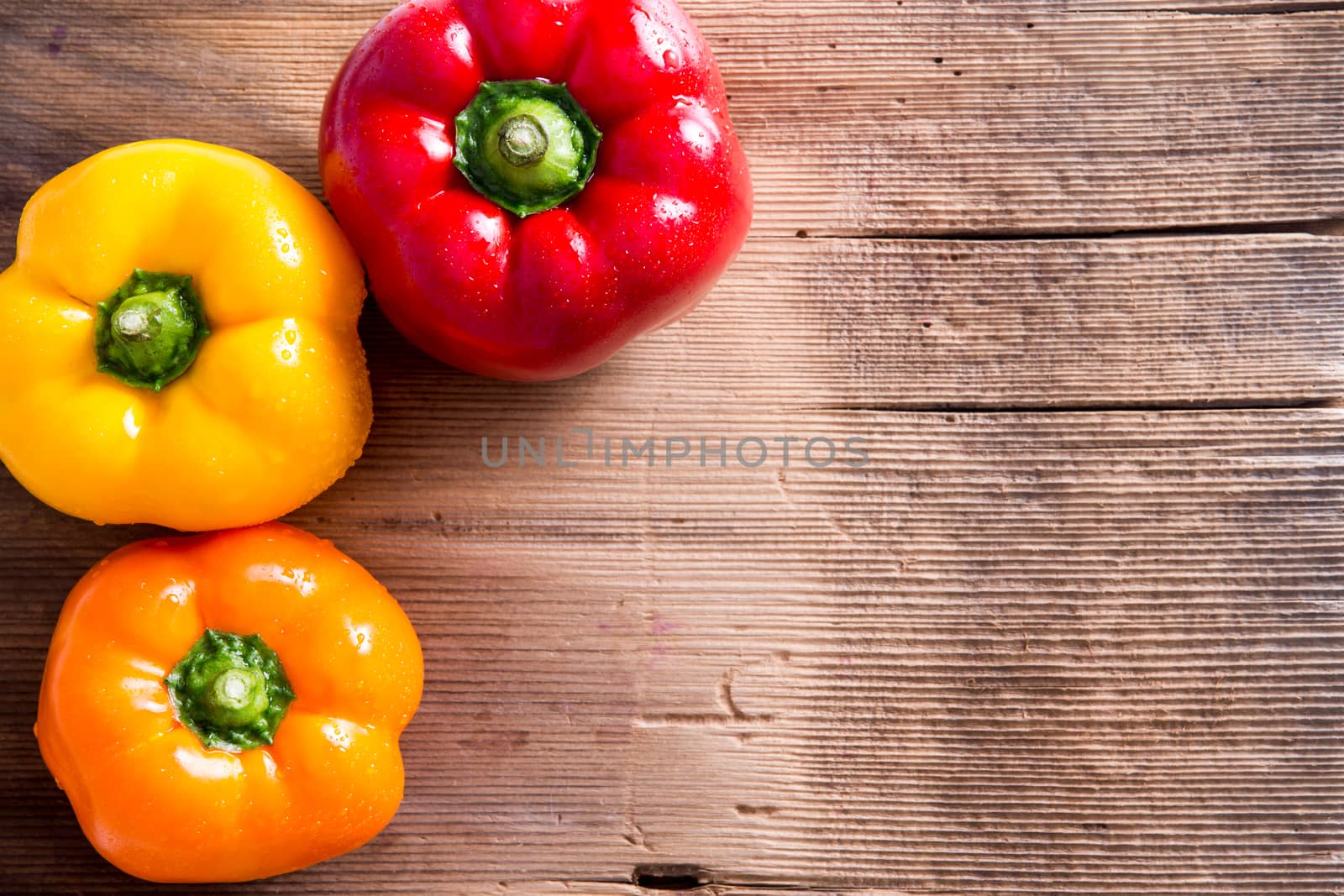 Three Fresh Bell Peppers in Red, Yellow and Orange on Top of Wooden Market Table with Copy Space for Texts. Captured in High Angle View.