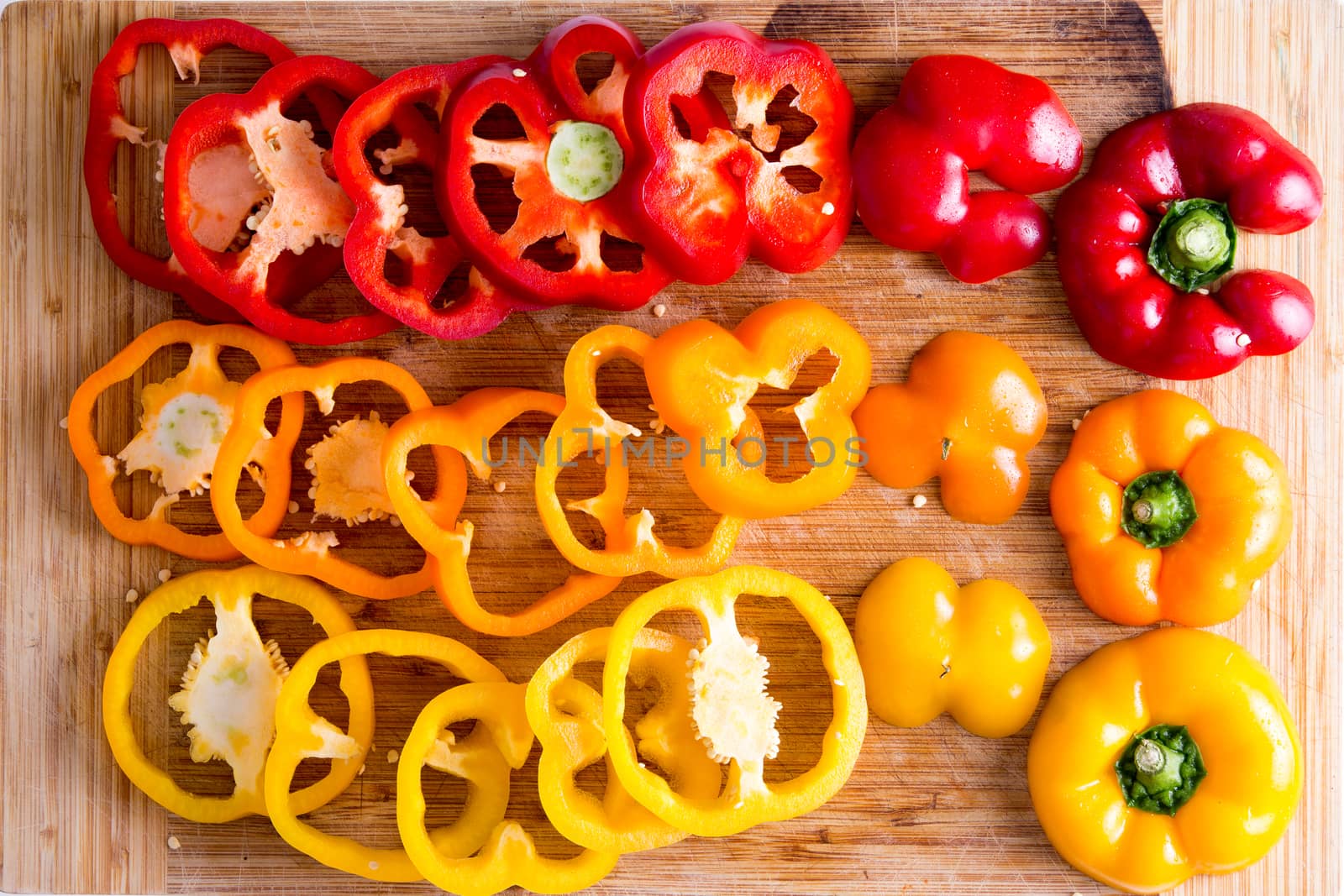 Close up Thin Slices of Red and Yellow Fresh Bell Peppers on Top of a Wooden Chopping Board, Captured in High Angle View.