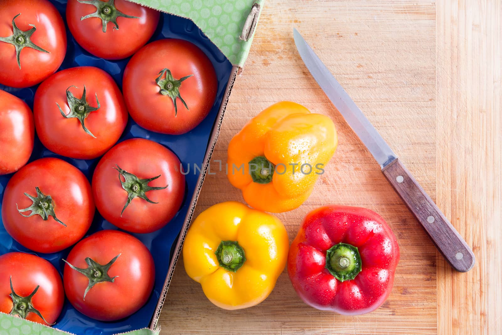 Fresh Red Tomatoes Tomatoes and Bell Peppers in Yellow and Red on Top of Wooden Chopping Board with Kitchen Knife.