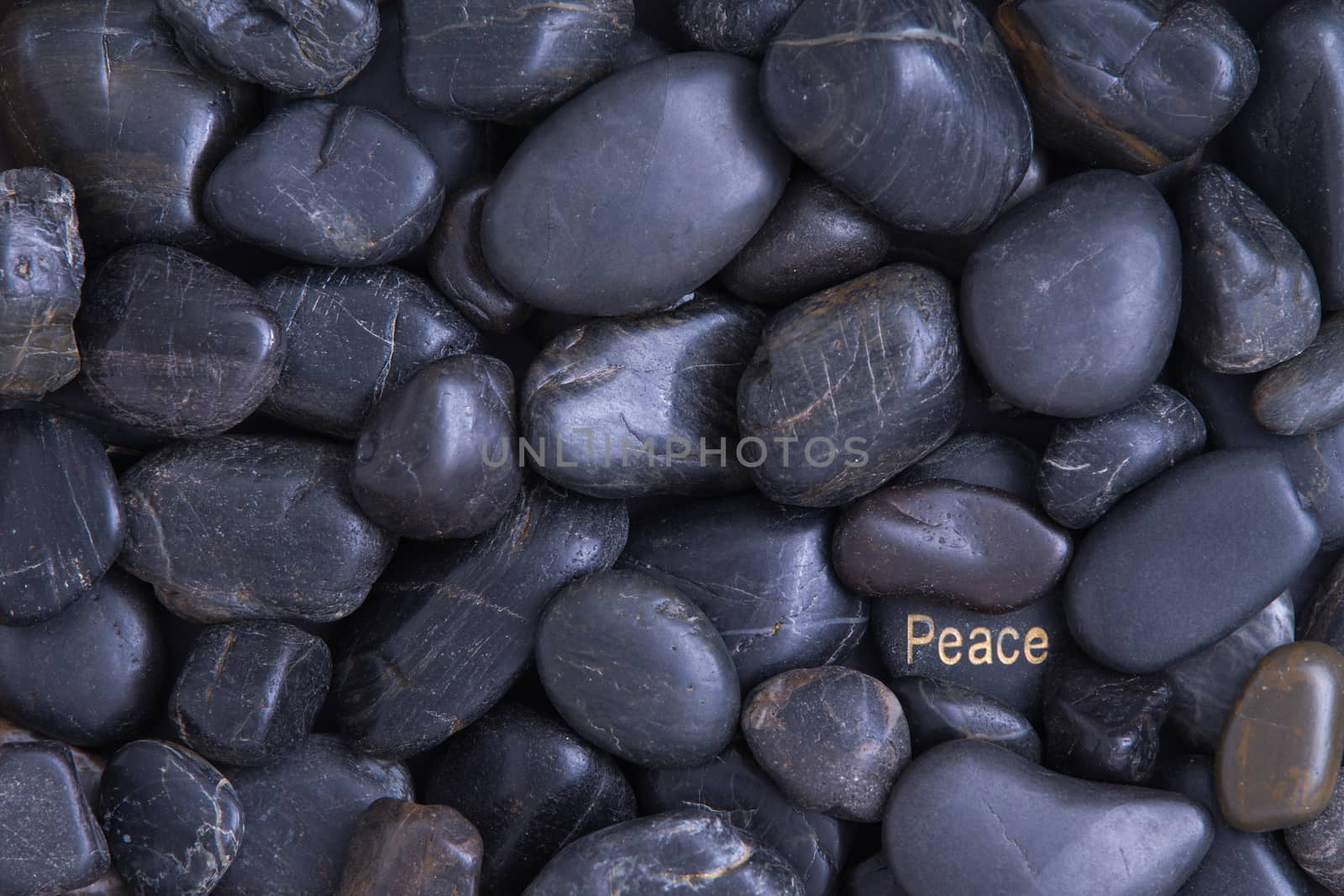 Smooth waterworn smooth black pebble full frame background with a Peace theme with one pebble in the lower right corner bearing the word in white