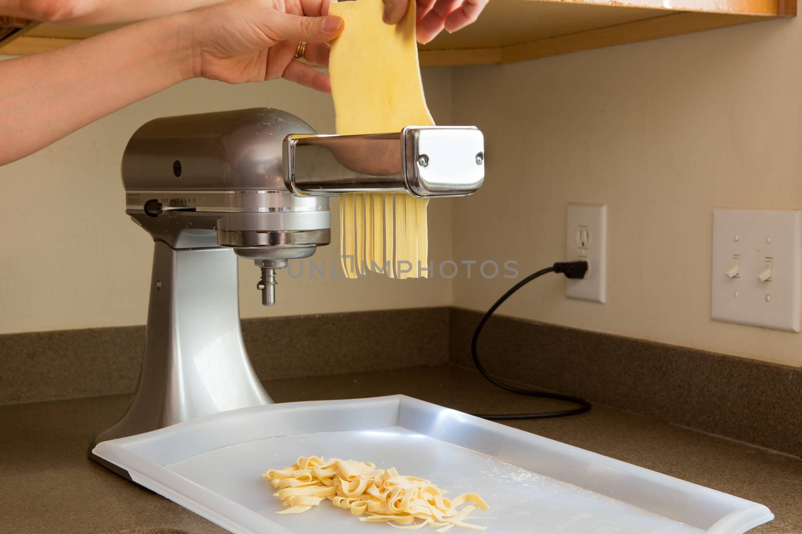 Chef preparing homemade fettuccine pasta feeding the rolled sheets of dough through the cutting machine in the corner of a kitchen, close up view of the dough and appliance