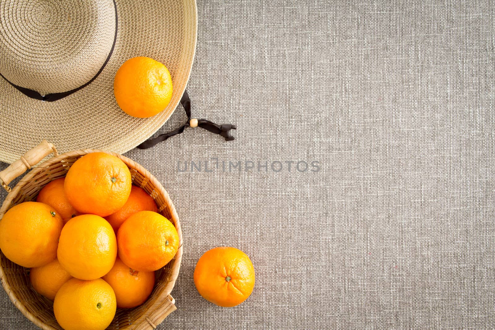 Harvest of farm fresh succulent ripe oranges with a straw sunhat direct from the farmer on a beige cloth background with copyspace viewed from overhead in a healthy diet and nutrition concept