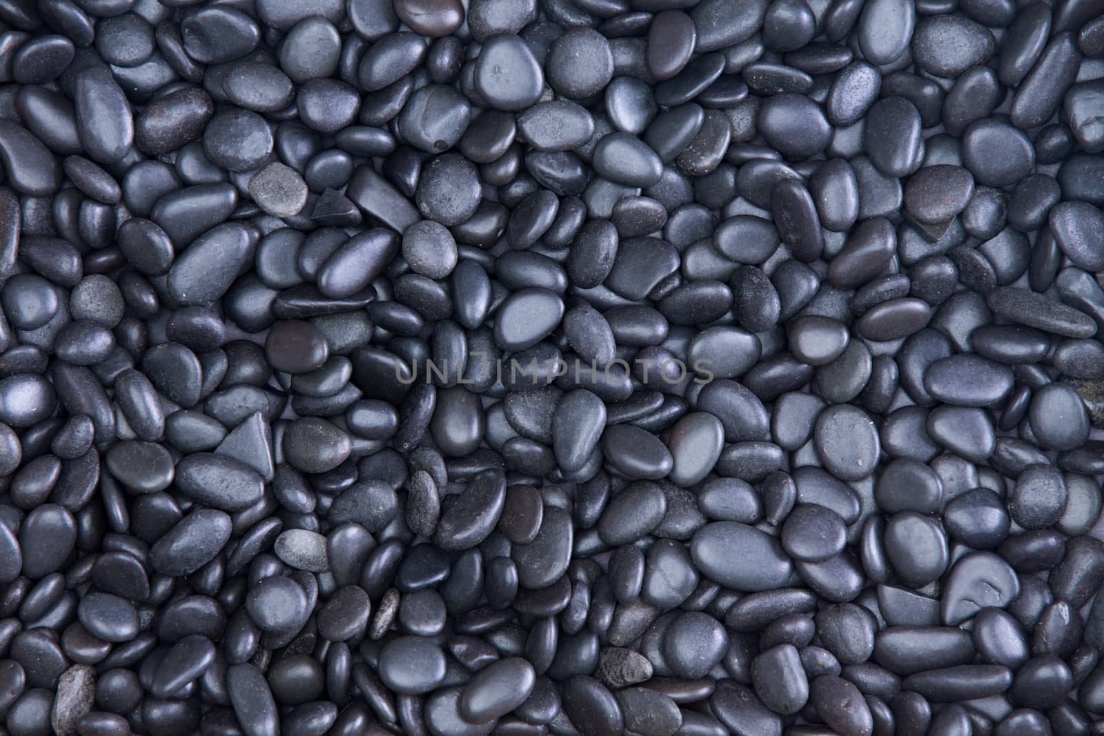 Background texture of small smooth waterworn black pebbles or stones for use in decor and garden landscaping, full frame close up view from above