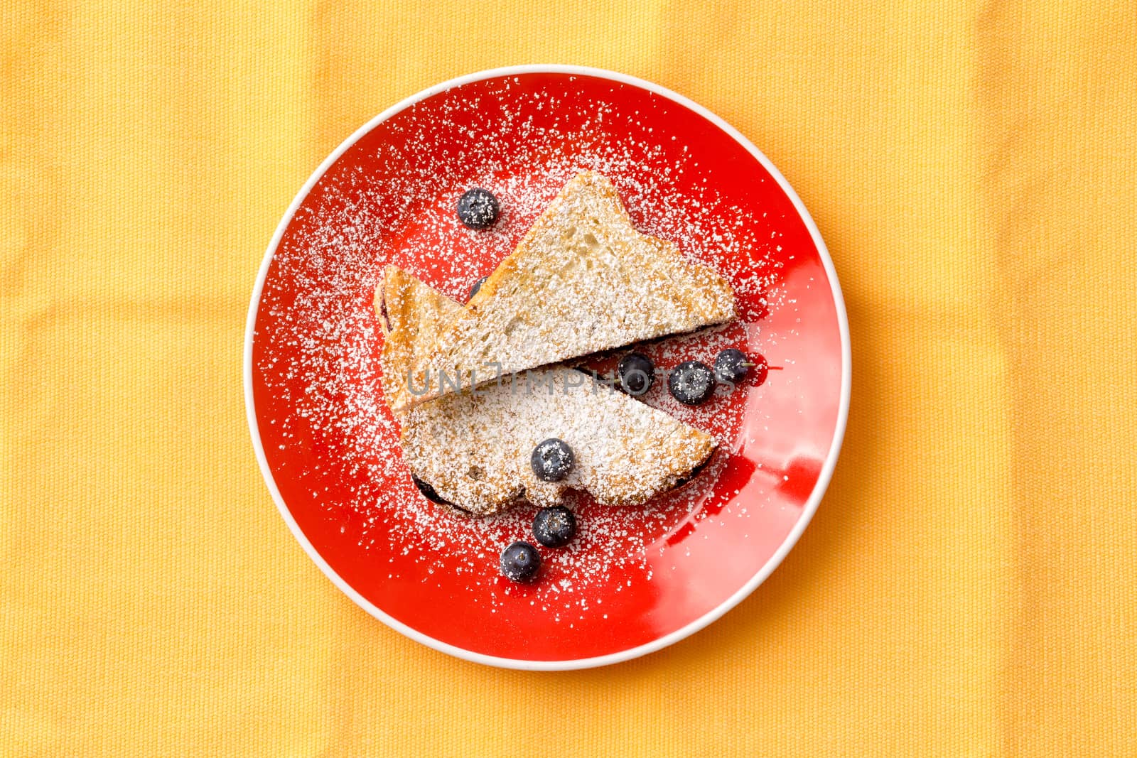 Aerial Shot of a Tasty French Toast Bread with Strawberry Jam Filling on Round Red Plate with Blueberry Fruits. Isolated on Yellow Background.