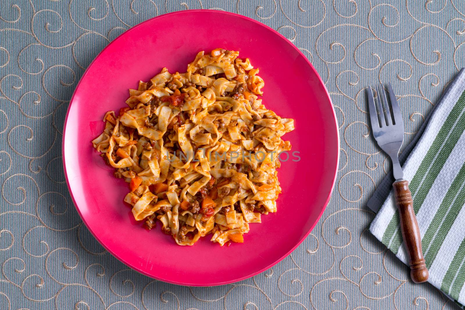 Plate of delicious homemade fettuccine pasta with a savory tomato and herb sauce served on a decorative whorled tablecloth, view from above