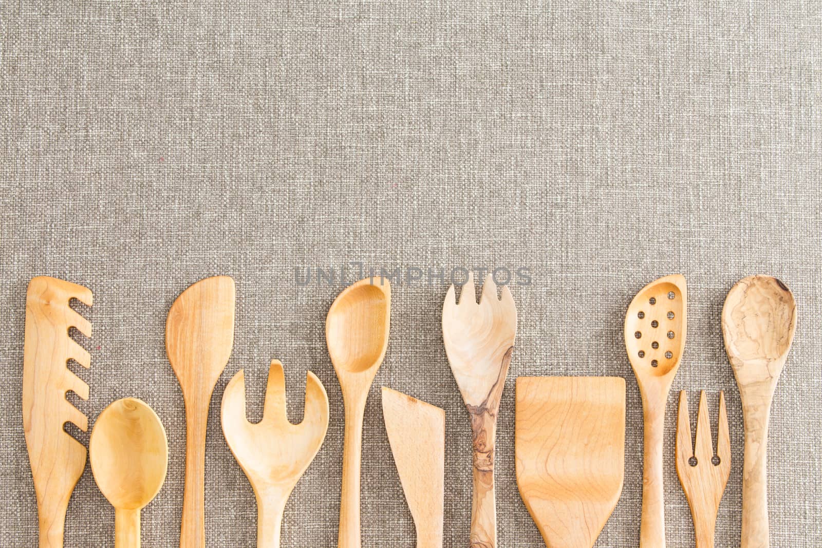 Border of wooden kitchen necessities with the heads of assorted utensils in a row along the bottom of the frame on a beige textile background with copyspace