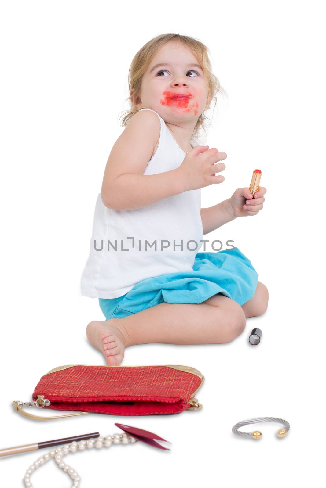 I didn't do it fun concept with a naughty little girl with her mouth smeared with lipstick surrounded by her mother's scattered cosmetics looking upwards with a guilty look, isolated on white