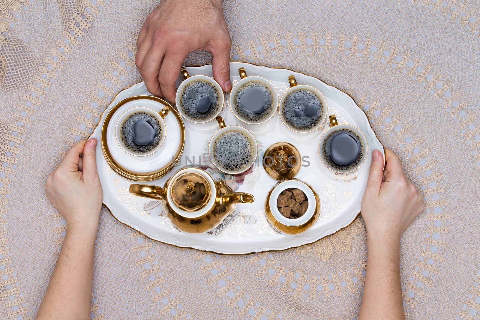 Six Small Cups of Turkish Coffee on a Tray Hold by Hand on Top of a White Table in High Angle View.