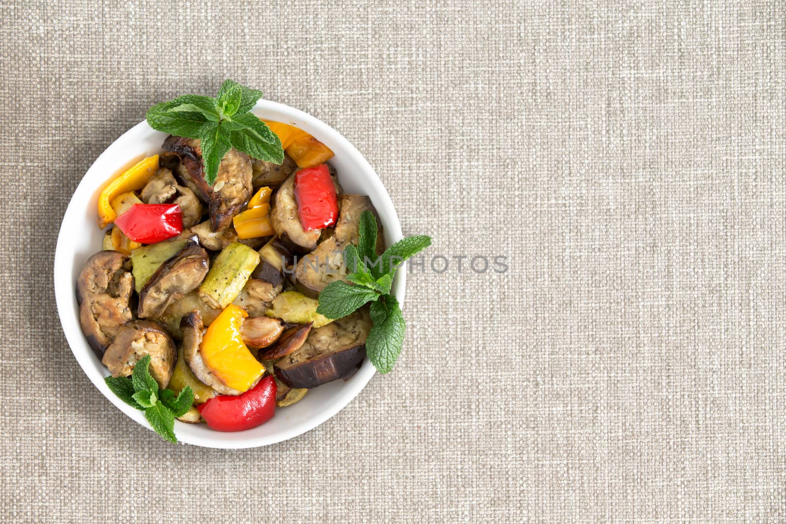 Plate of delicious grilled fresh vegetables prepared Turkish style with eggplant, zucchini and red and yellow sweet peppers, over head view on a beige cloth with copyspace