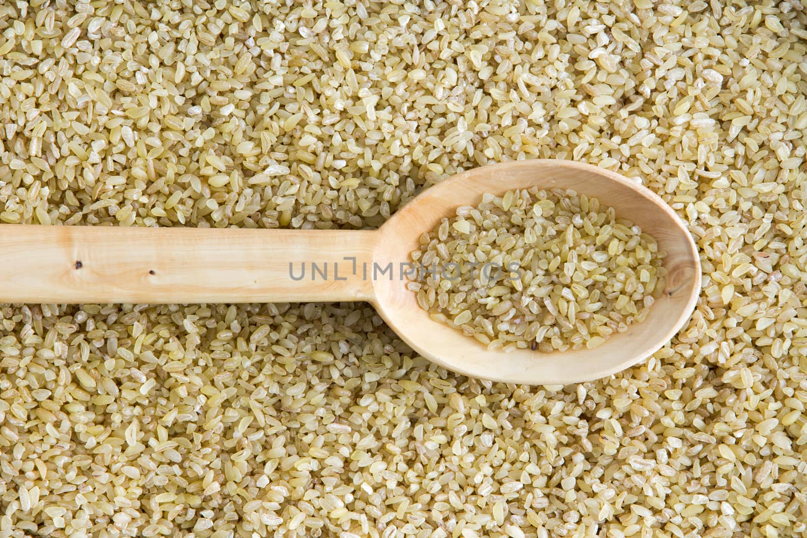 Background texture of cracked wheat with a centered rustic wooden spoon on crushed wheat grains pulverised to reduce cooking time