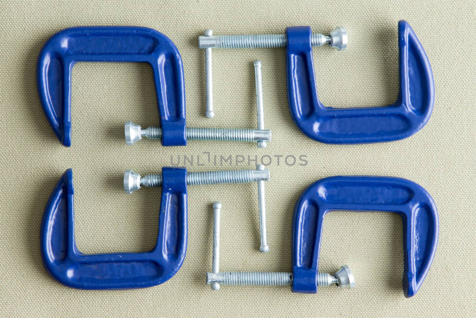 Four blue steel g-clamps neatly arranged on a grey background viewed from above in a DIY, renovation, repair and construction concept