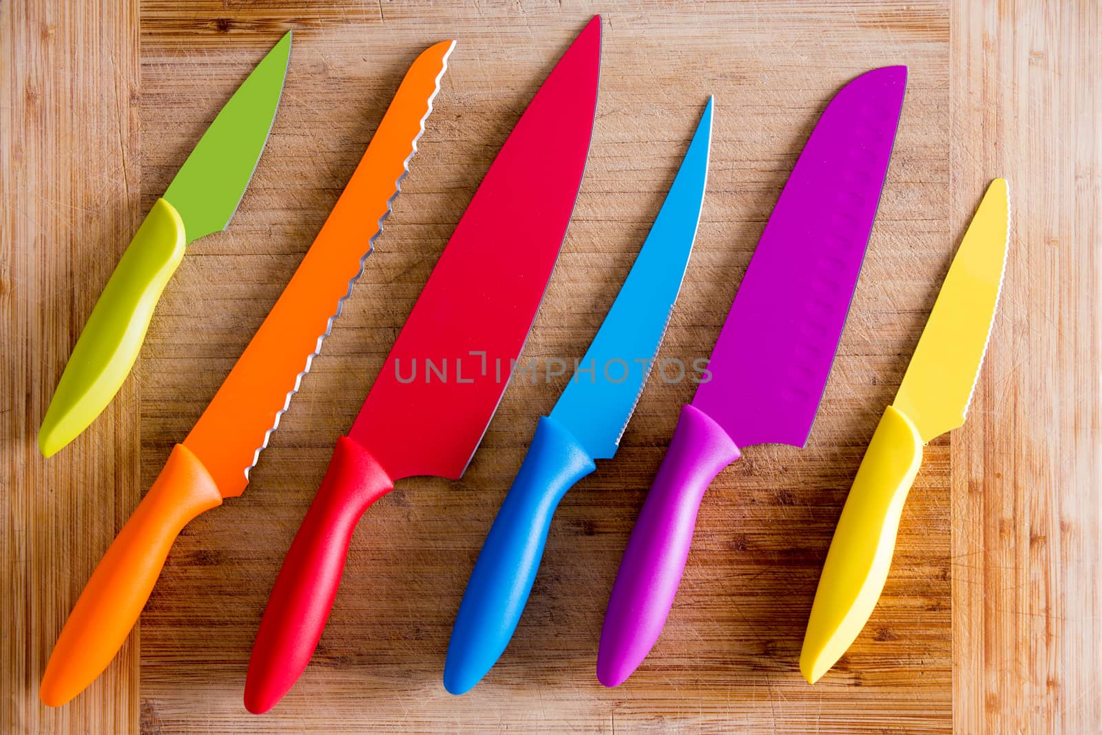 Close up Colorful Kitchen Knives with Different Purposes on Top of a Wooden Cutting Board, Captured in High Angle View.