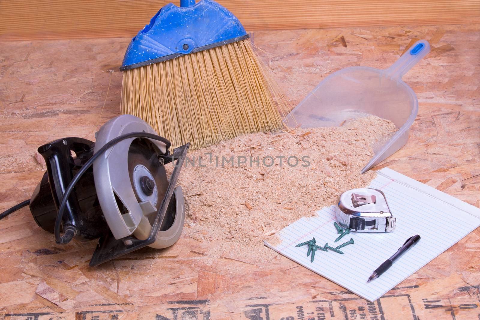 Handheld circular saw with sawdust, brush and pan lying on the floor with a tape measure, pen and nails on a page of paper in a concept of the mess and aftermath of carpentry