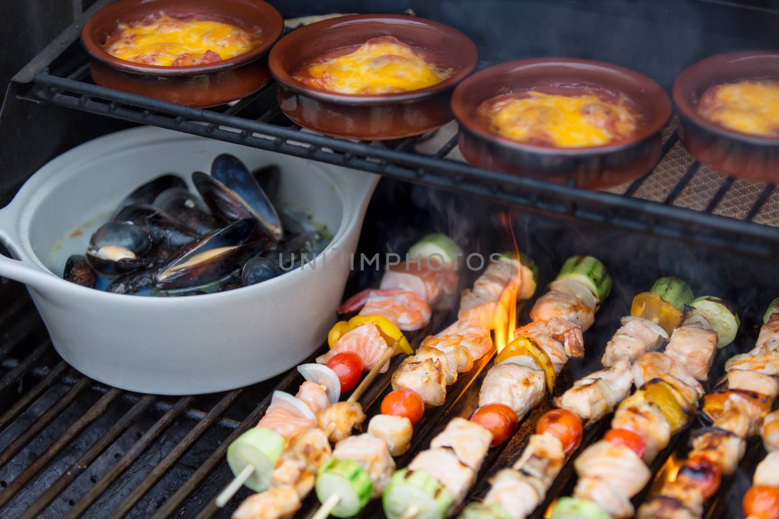 Delicious seafood outdoor meal at the BBQ with grilled salmon shish kebabs, marine mussels and individual pots of sausage stew, close up view on the grill