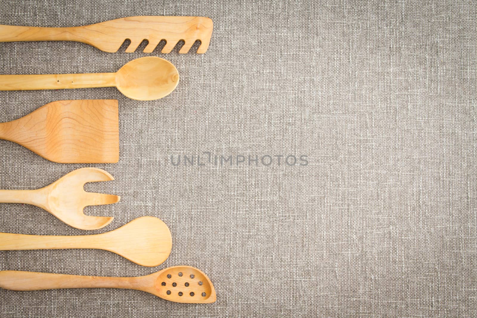 Wooden cooking utensils for food preparation arranged in a curving row as a decorative side border on a neutral beige linen textile with copyspace