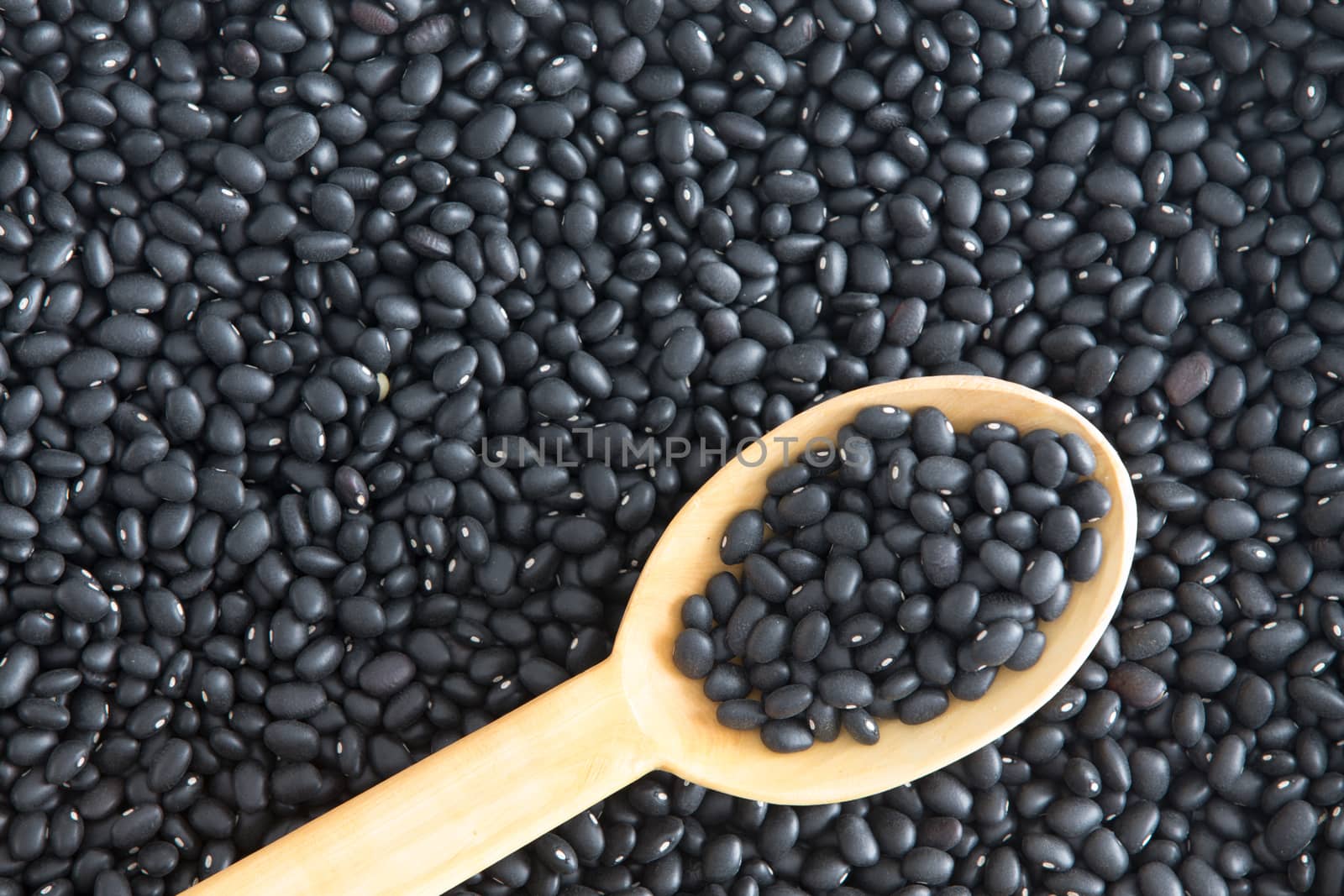 Bacground texture of healthy black beans, Phaseolus vulgaris, a variety of kidney bean with a rustic wooden kitchen spoon lying diagonally angled in the frame