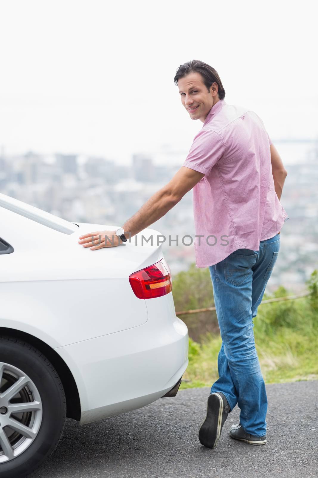 Smiling man standing next to his car at the side of the road