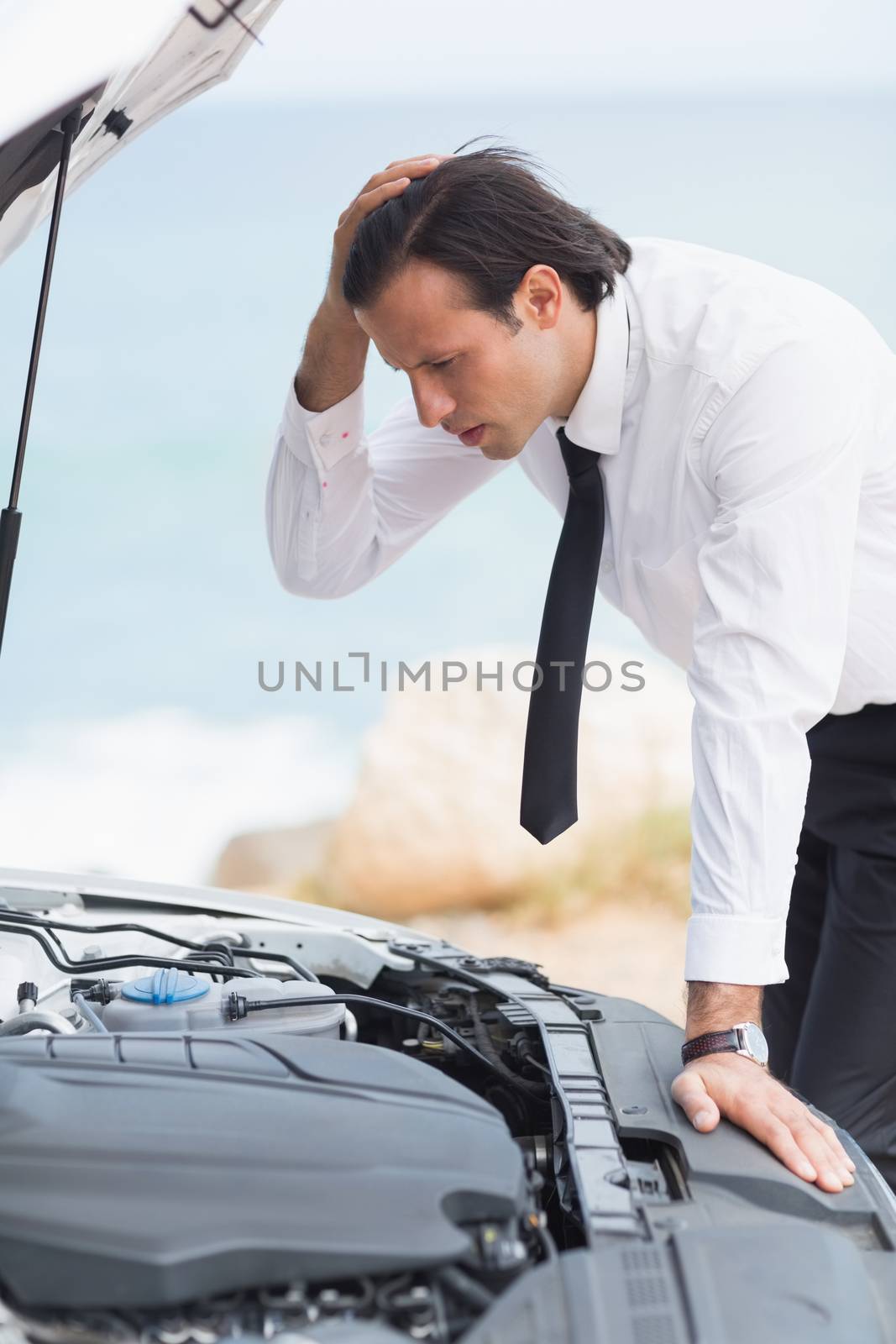 Stressed businessman looking at engine of his car