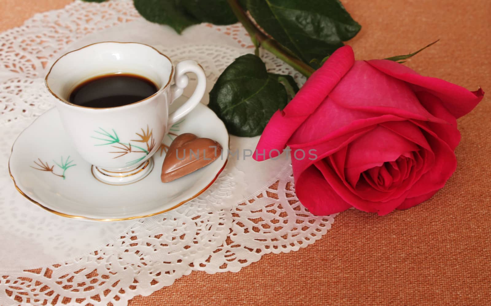 Still Life with cup of coffee and a pink rose on a lace salfete