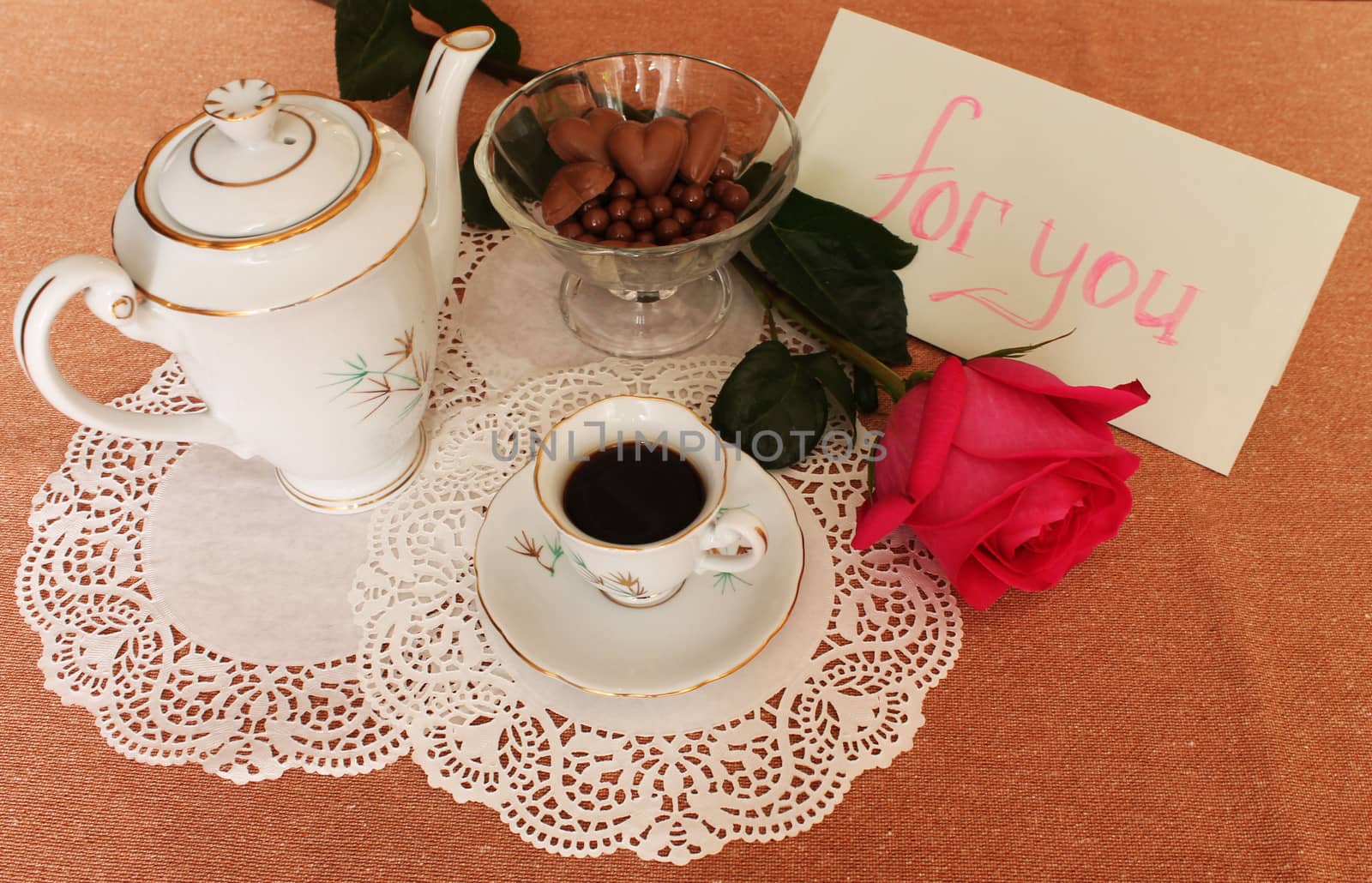 Still Life with cup of coffee, coffee pot, vase with sweets and rose on lace salfete