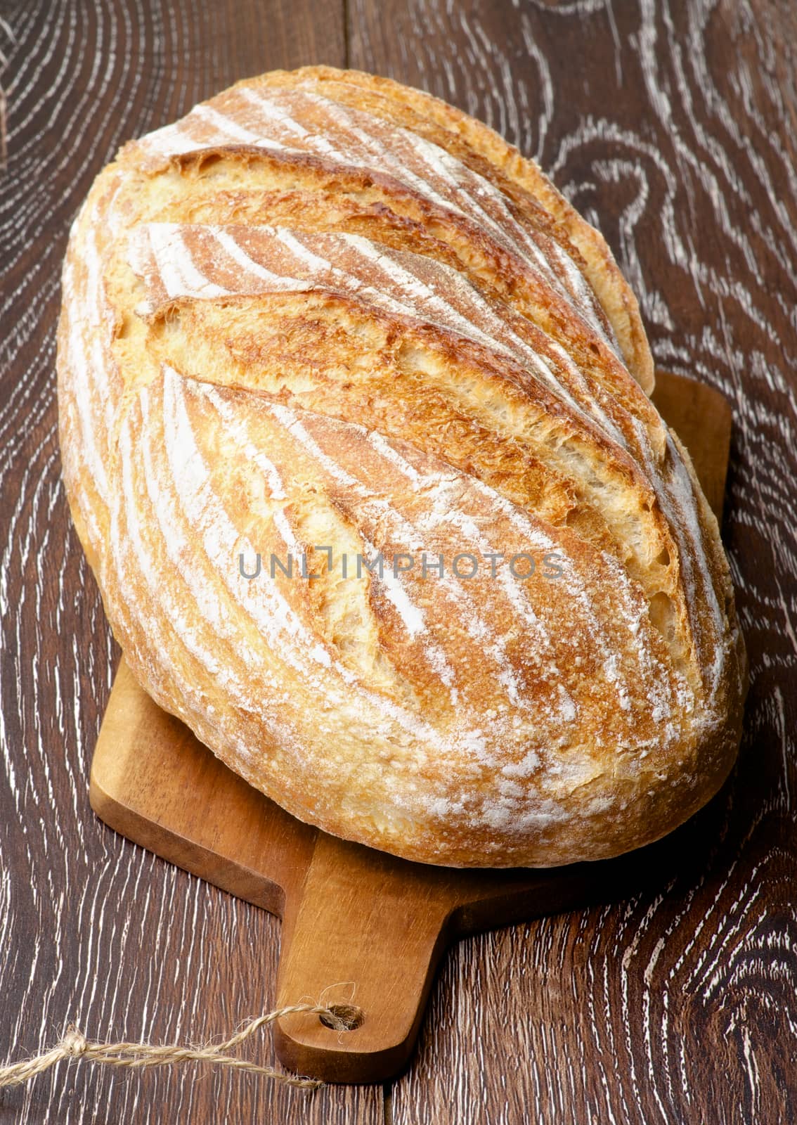 Big Loaf of Homemade Wheat Bread Full Body on Wooden Cutting Board closeup on Dark Wooden background