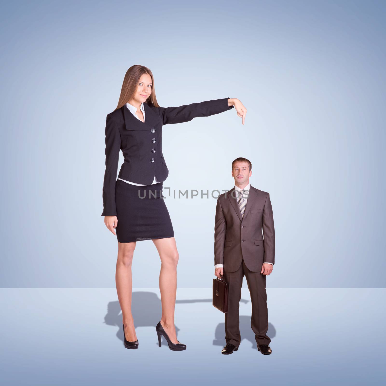 Smiling Young Businesswoman Pointing to small Businessman. Blue background