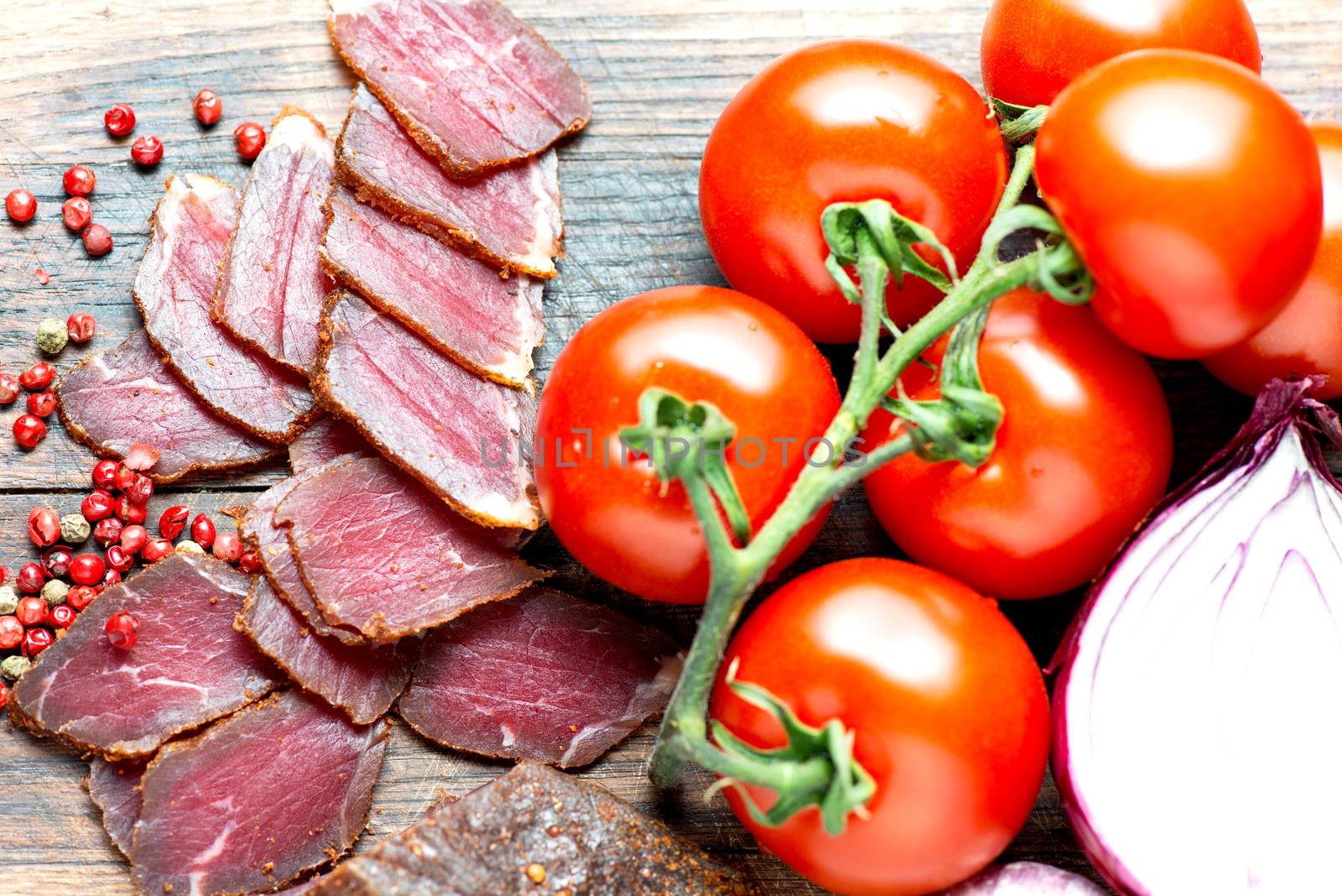 Prosciutto slices, pepper corn and tomatoes on wooden table