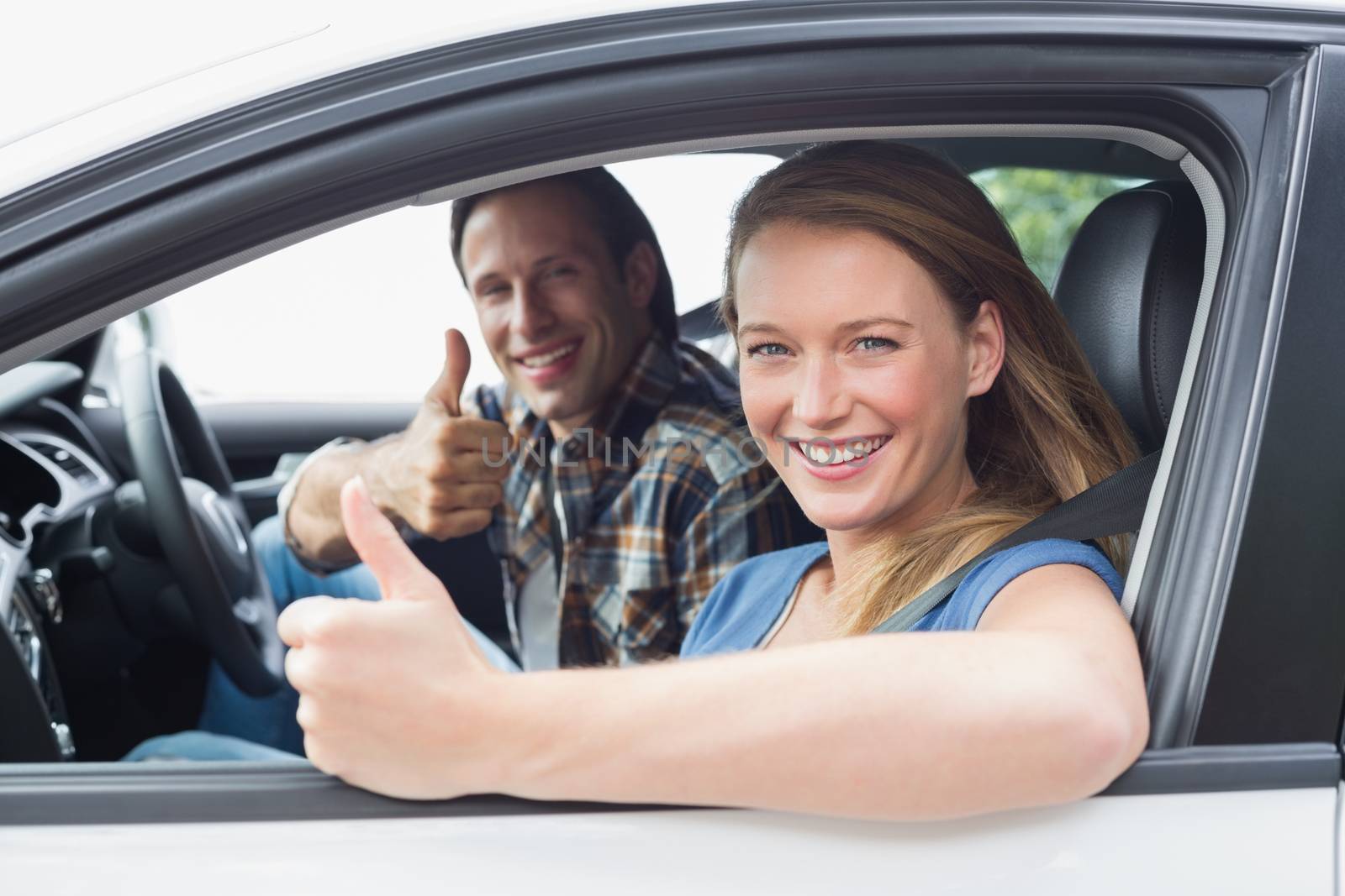 Couple smiling at the camera with thumbs up in their car 