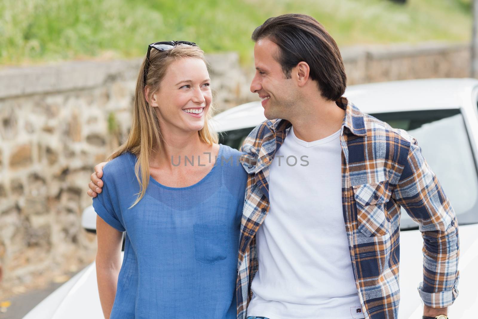 Couple smiling each other leaning on their car 