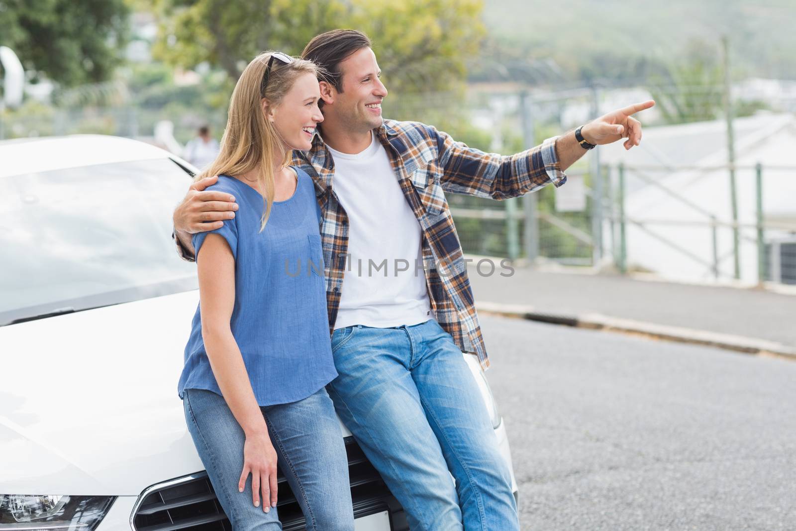 Smiling couple leaning on the bonnet of their car 