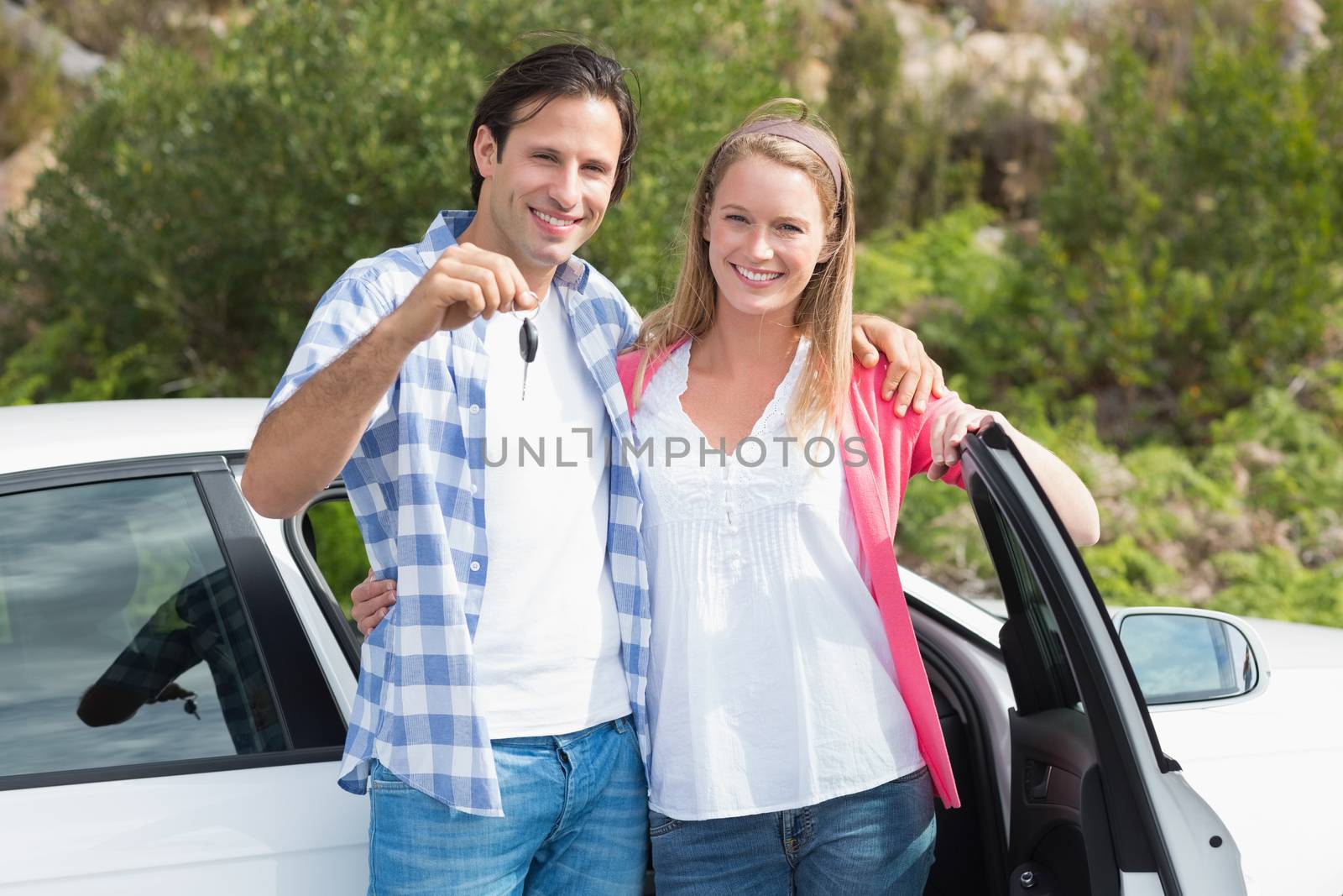 Young couple smiling at the camera outside their car