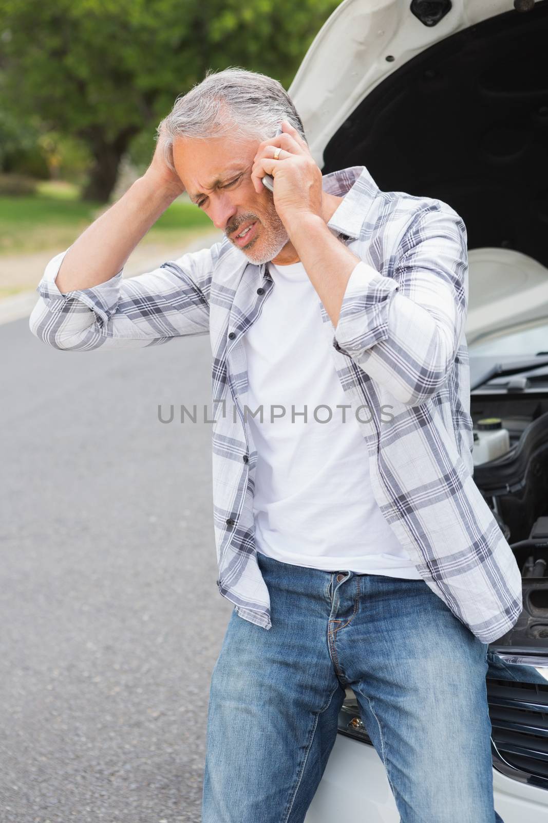 Stressed man calling beside his broken down car 
