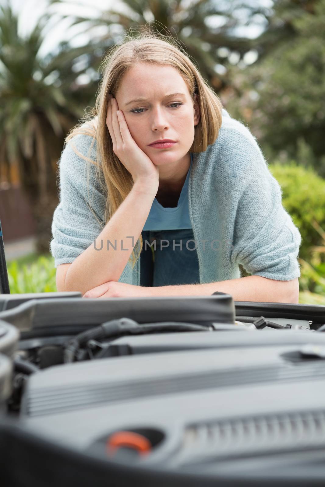 Thoughtful woman looking at engine of her car