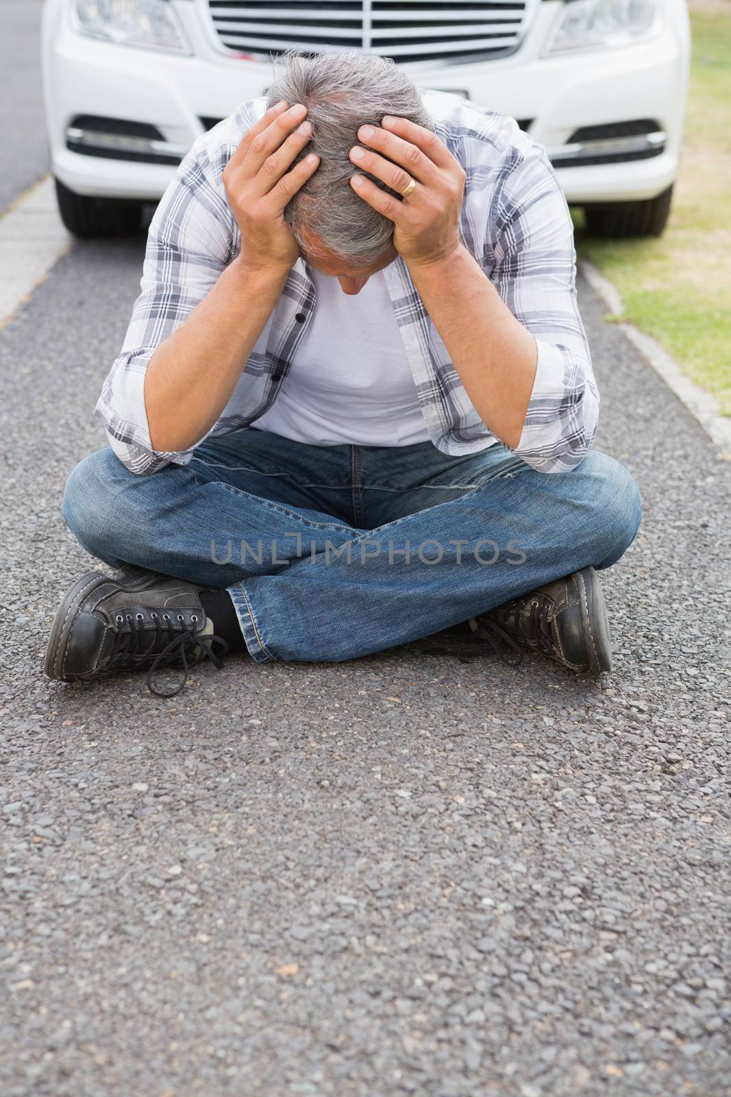 Stressed man sitting on the ground beside his car 