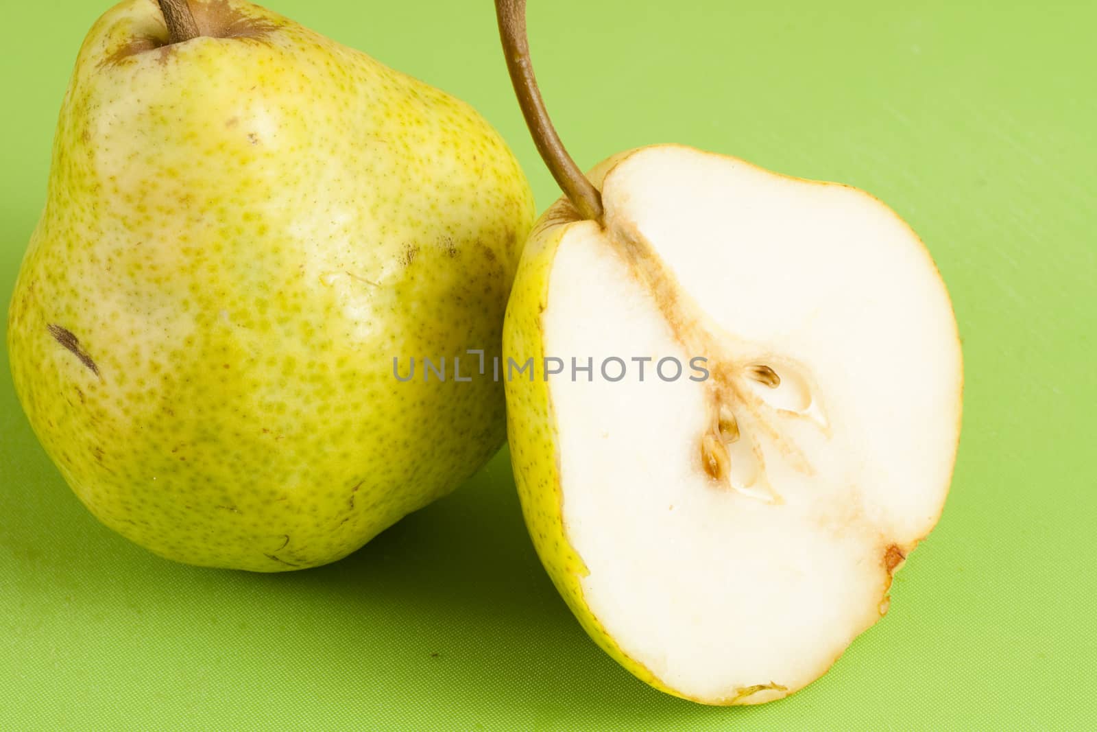 green pear cut in half on a green floor and a whole pear