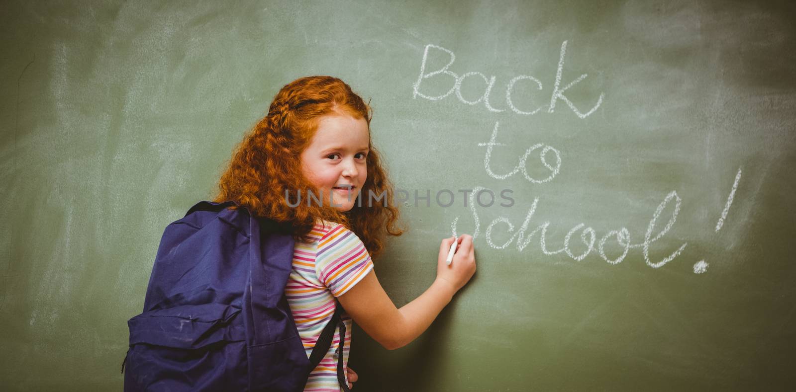 Portrait of cute little girl writing on blackboard in the classroom