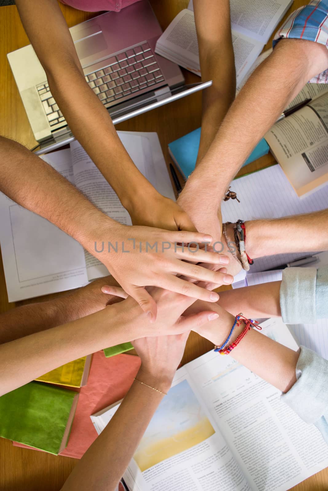 Students placing hands together over library table by Wavebreakmedia