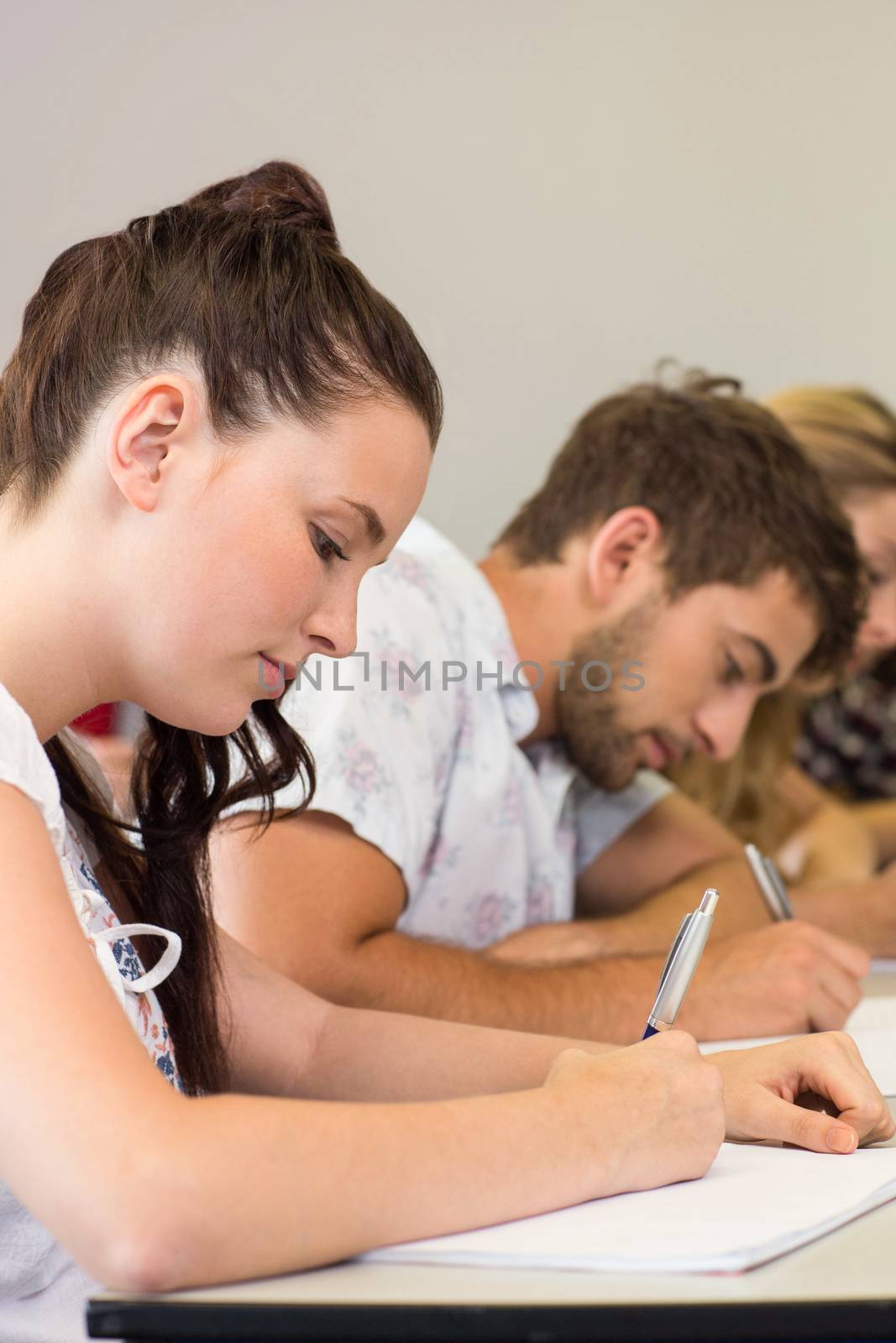 Side view of students writing notes in classroom