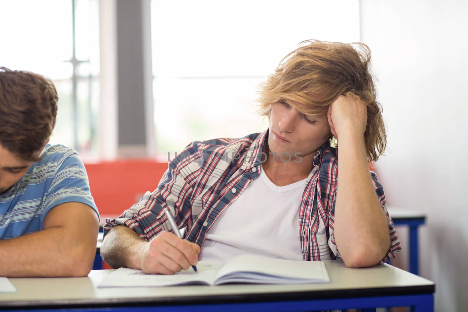 Portrait of male student writing notes in classroom