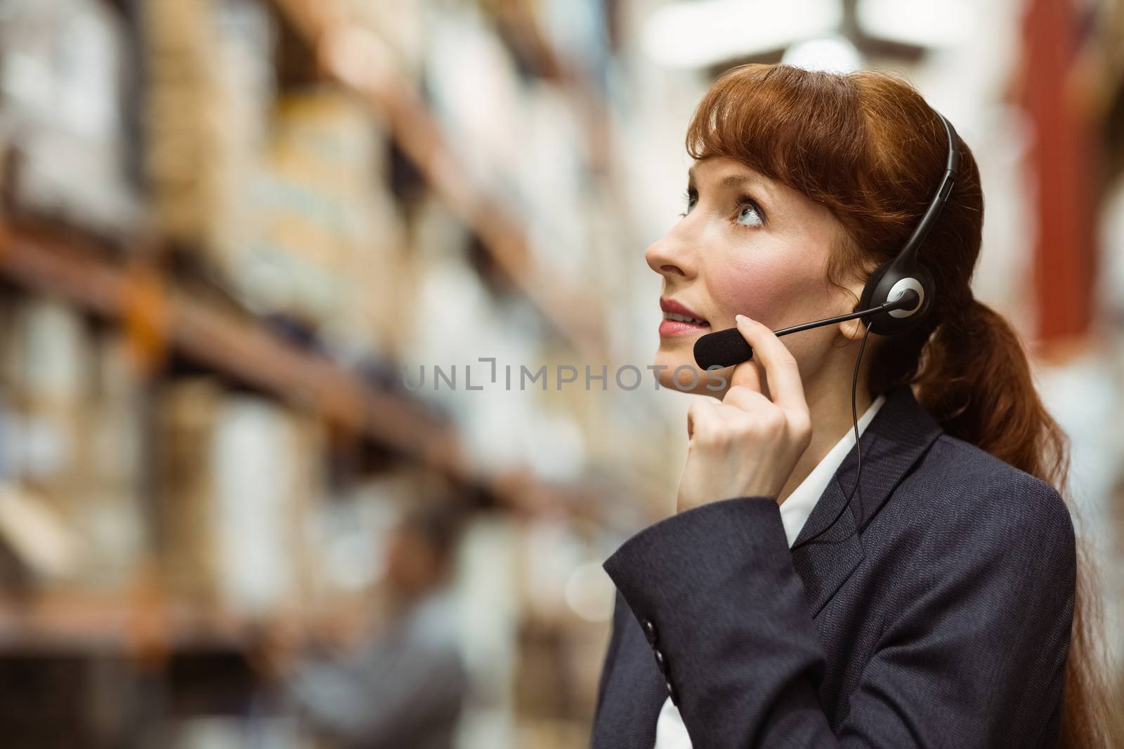 Pretty businesswoman speaking in a headset in a large warehouse