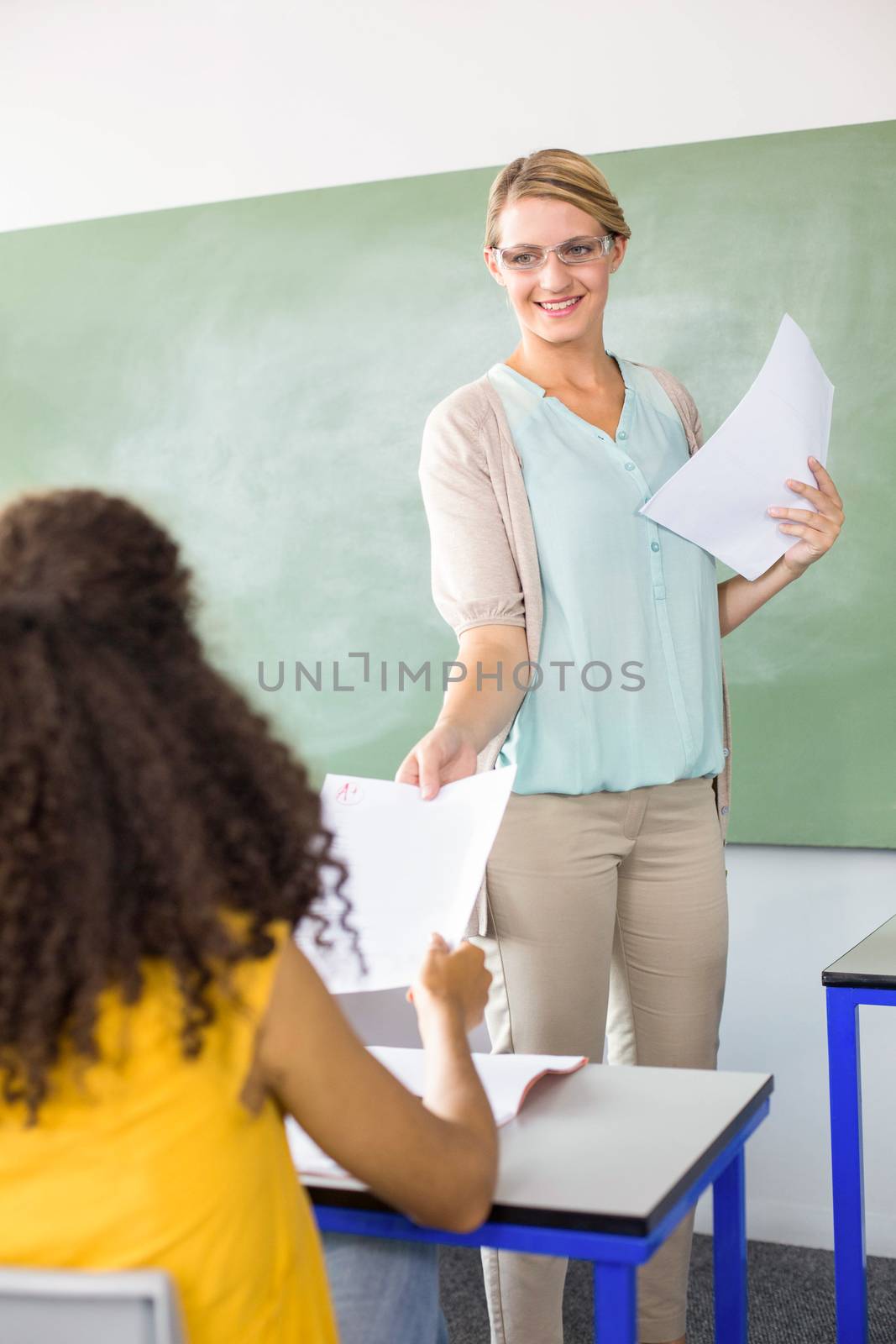 Female teacher handing paper to student in the class