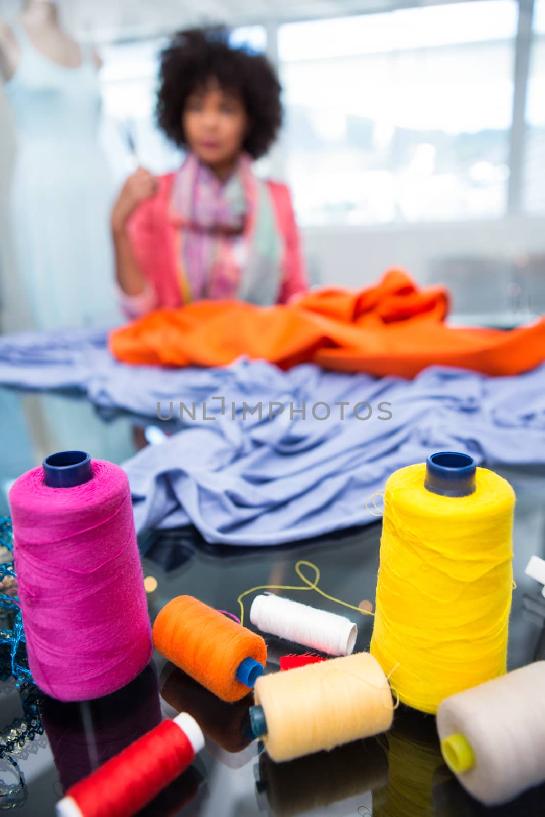 Close up of threads on table with female fashion designer in background