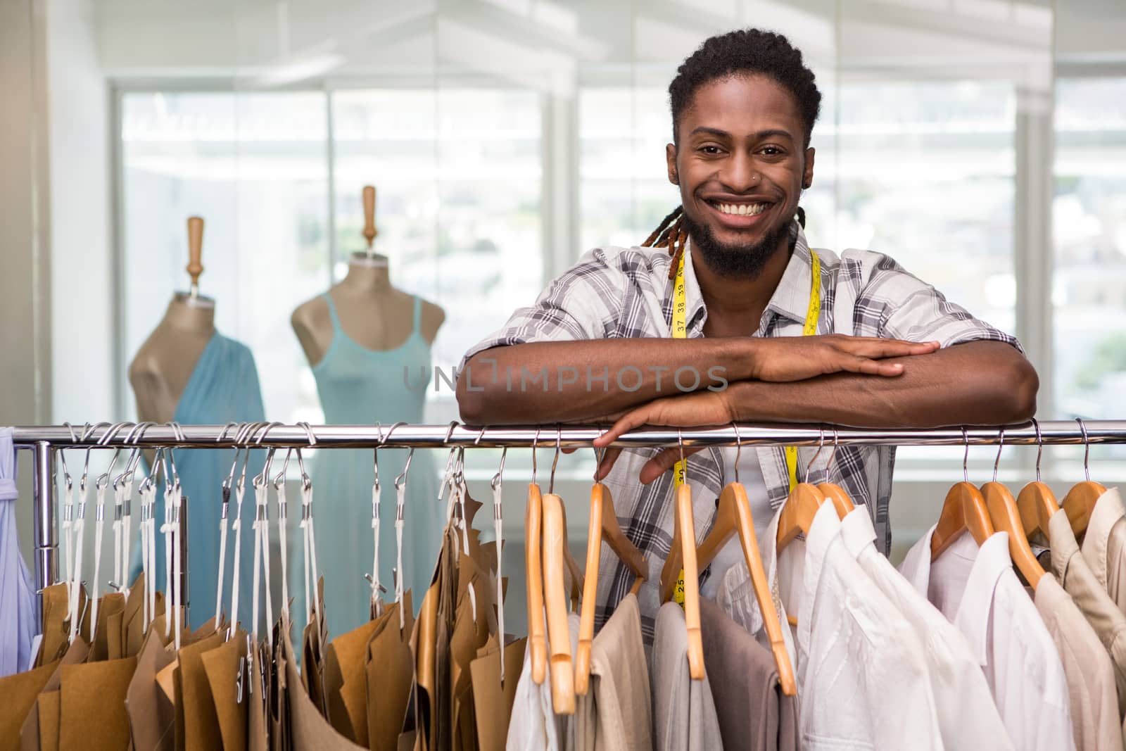 Portrait of male fashion designer leaning on rack of clothes