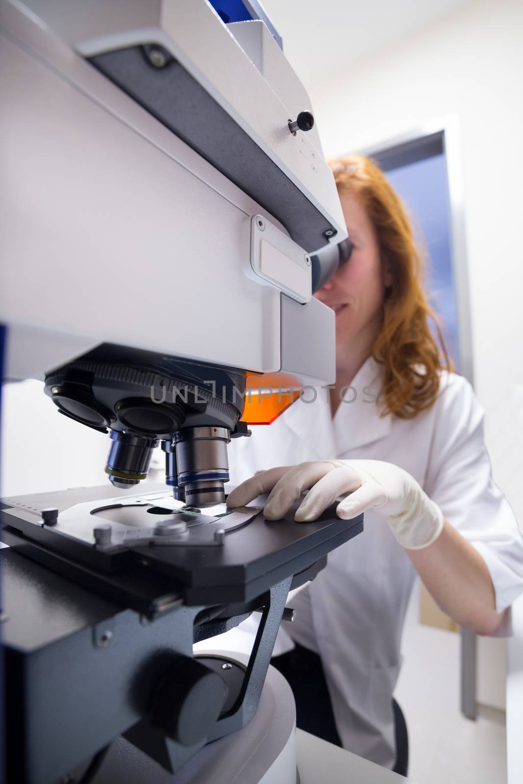 Female scientist microscoping on hi-tec fluorescent microscope. . Health care professional in hes working environment.